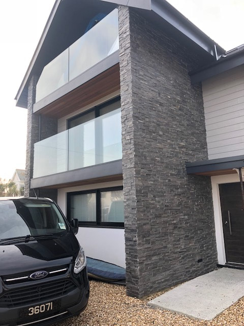 Norstone Charcoal Slimline Stone Veneer Panels used on an exterior feature wall on a residential home in the UK with luxury touches like a clear glass balcony railing